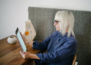 Older woman reading a bright tablet at a table